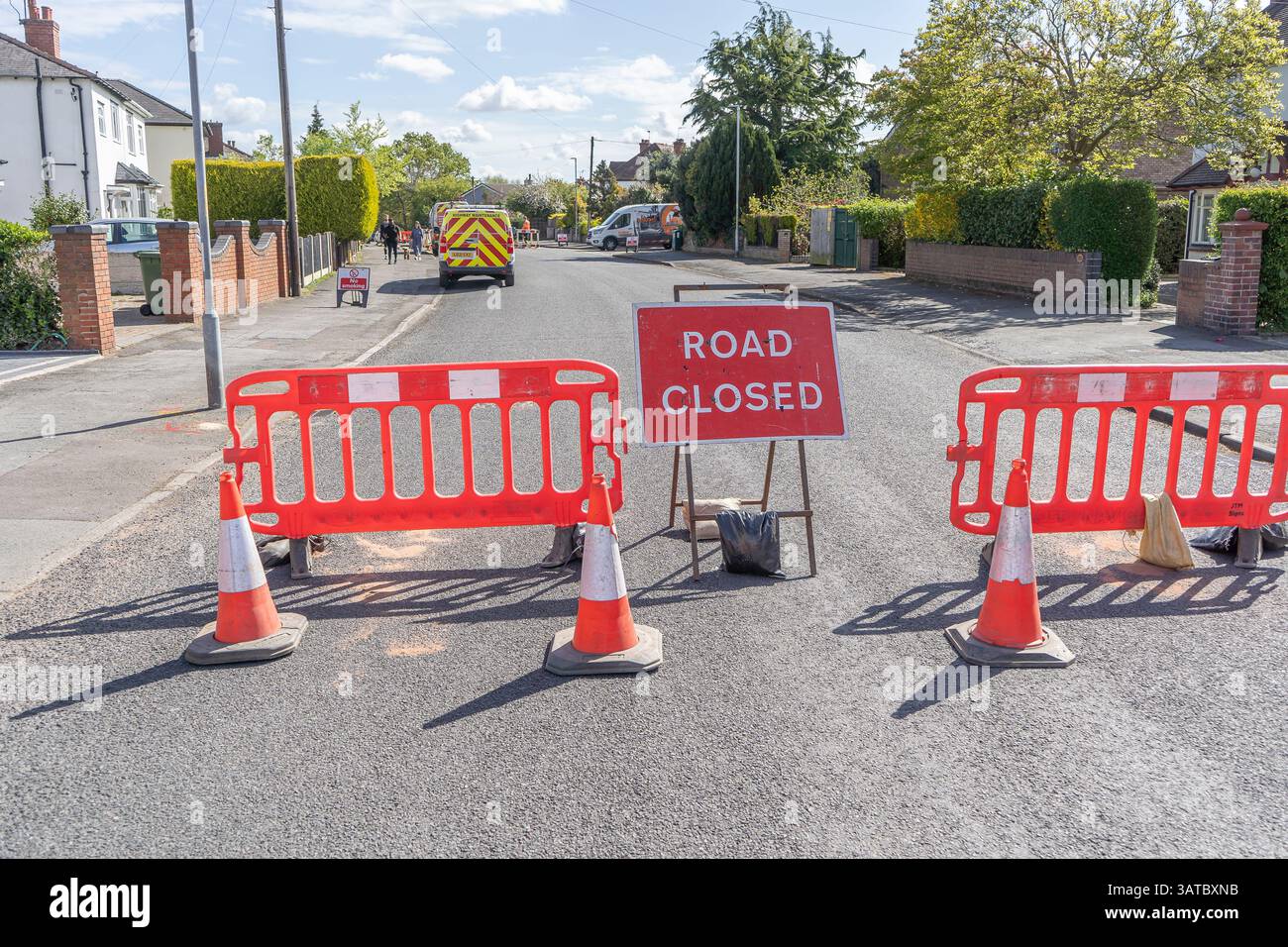 Segnaletica STRADALE rossa CHIUSA con barriere che bloccano una strada residenziale con furgoni parcheggiati dietro. Lavori stradali locali durante il sole primaverile. Foto Stock