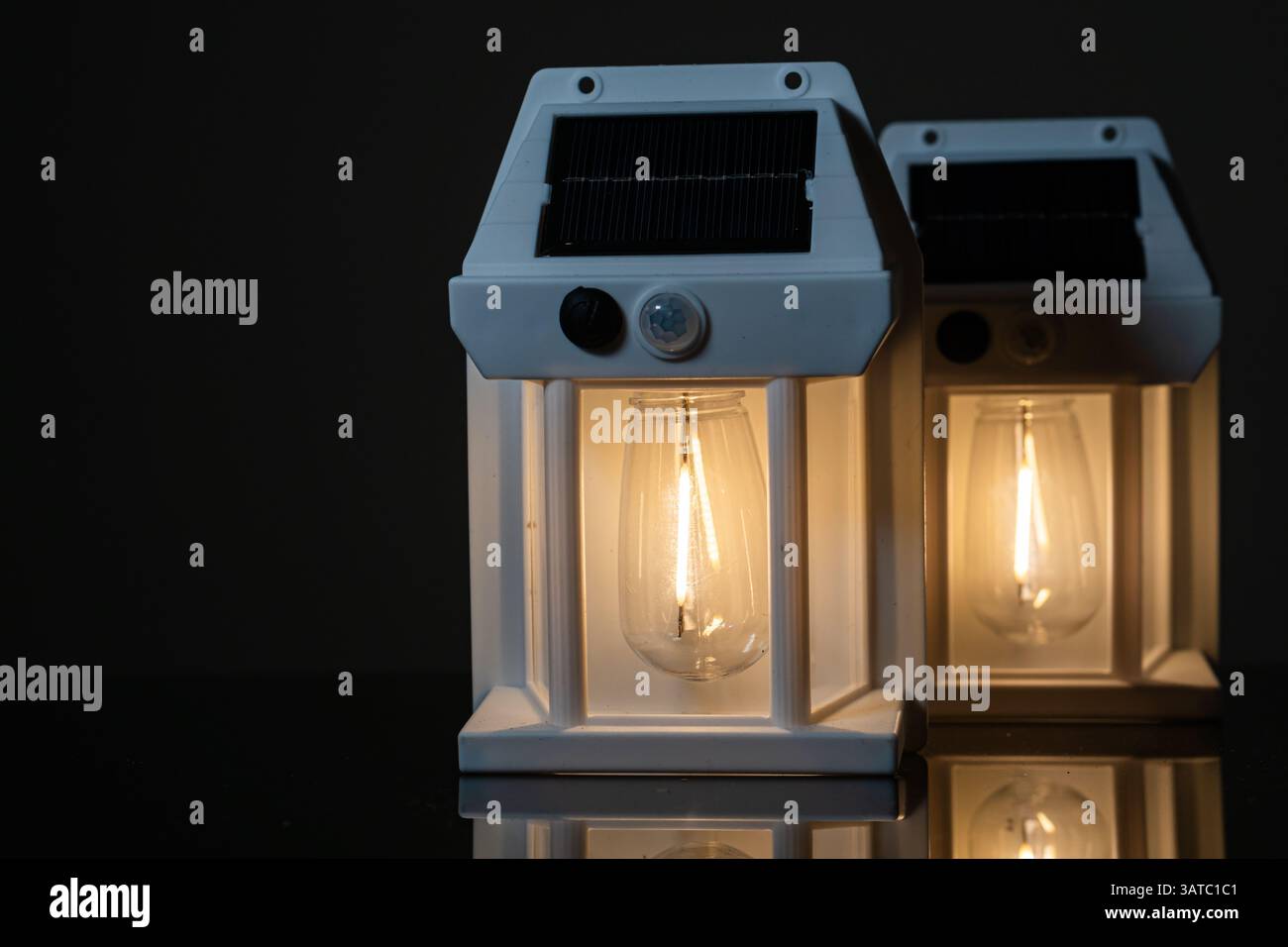 Due lanterne alimentate a energia solare con lampadine calde incandescenti, disposte su uno sfondo scuro. Le lanterne hanno un design moderno che mostra la loro gla trasparente Foto Stock