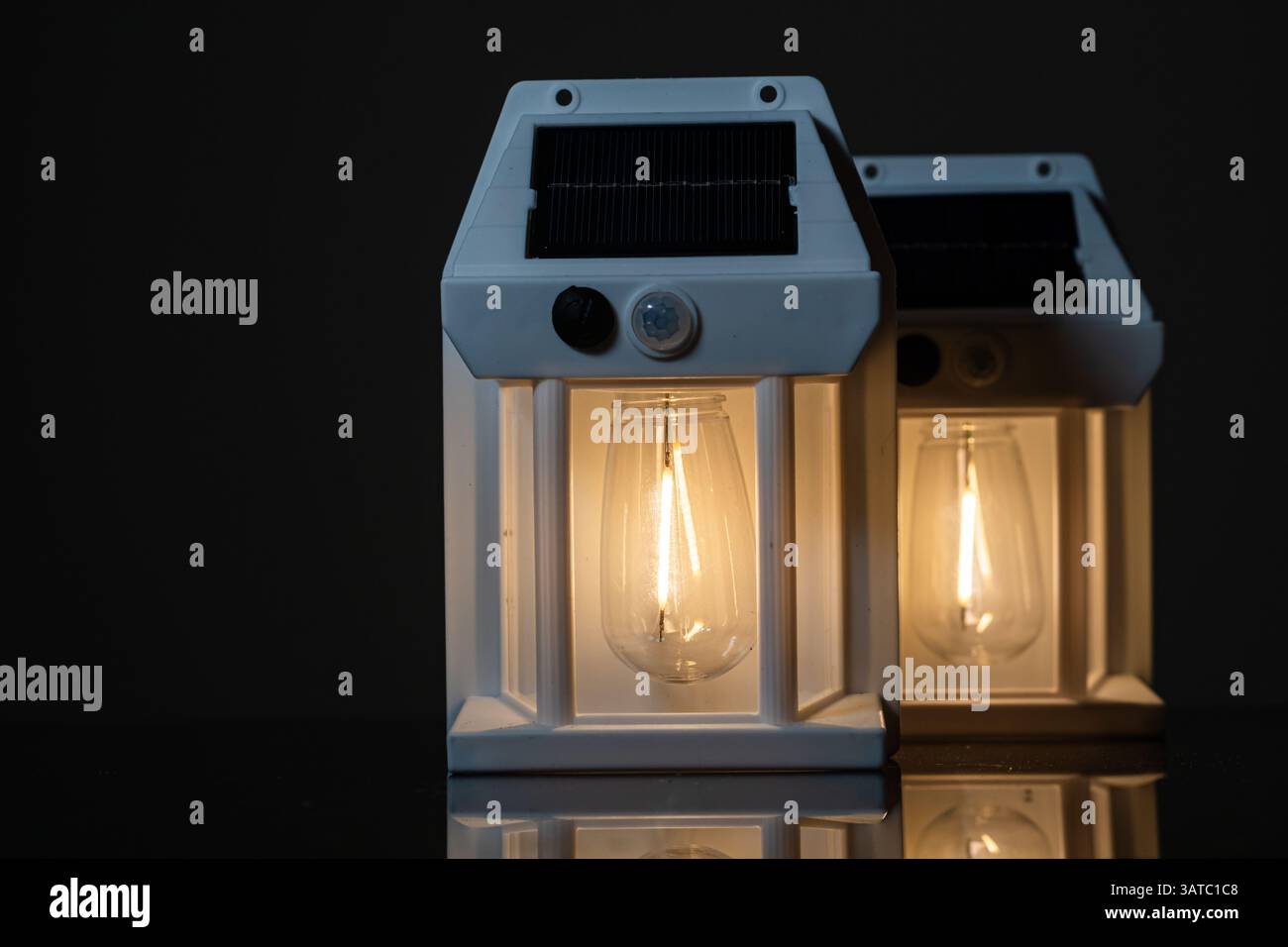 Due lanterne alimentate a energia solare con lampadine calde incandescenti, disposte su uno sfondo scuro. Le lanterne hanno un design moderno, ideale per l'illuminazione esterna o de Foto Stock