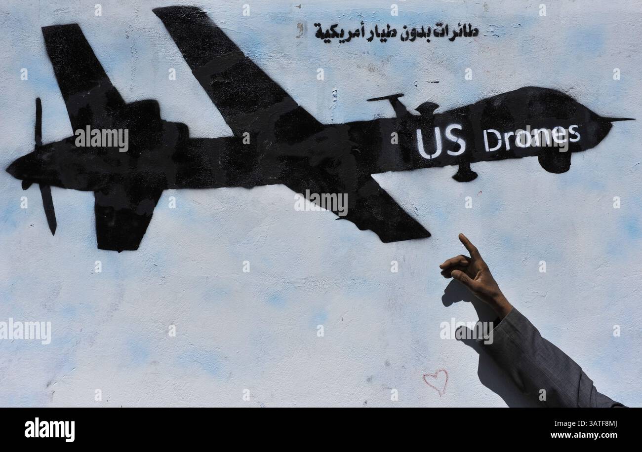 6 novembre 2013 - Sana'a, Yemen - Un uomo yemenita indica la grafica dipinta sul muro contro i droni statunitensi utilizzati nello Yemen durante una campagna sul muro chiede al governo degli Stati Uniti di fermare i suoi attacchi con i droni in questo paese povero. Da quando gli Stati Uniti hanno lanciato il suo primo attacco letale con droni in Yemen nel 2002 fino alla metà del 2013 come parte della sua politica antiterrorismo, il programma si è notevolmente ampliato. I gruppi per i diritti umani hanno criticato la mancanza di trasparenza e gli standard fondamentali del diritto internazionale che inquadrano questa guerra segreta. Lo sciopero dei droni del 92 in Yemen ha causato tra i 680 e i 880 yemeniti uccisi, tra cui 60 civili. (Credito Foto Stock