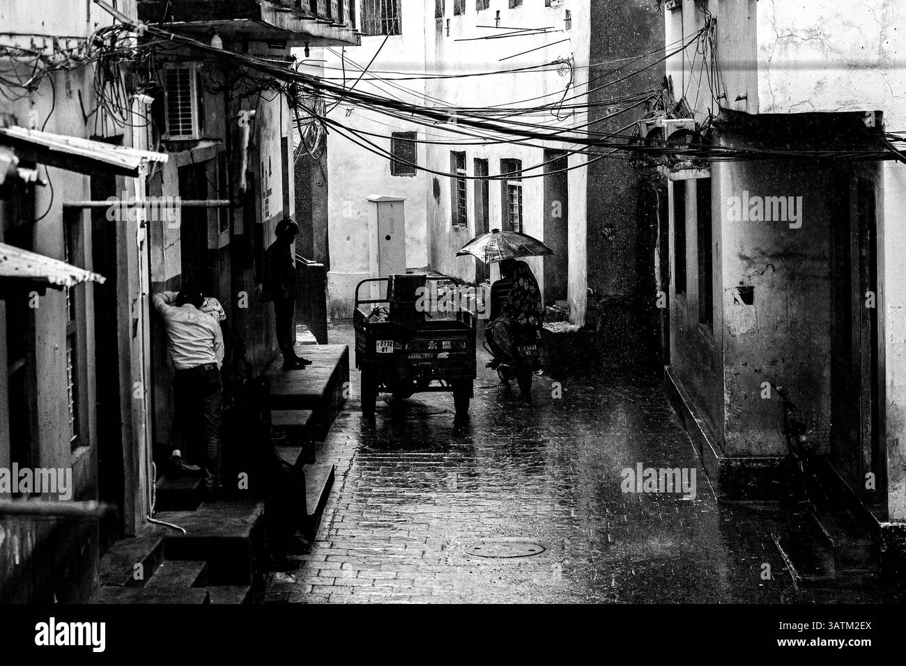 Una scena di strada con gente che si ripara dalla pioggia torrenziale nella stagione delle piogge a Stone Town, Zanzibar, Africa Foto Stock