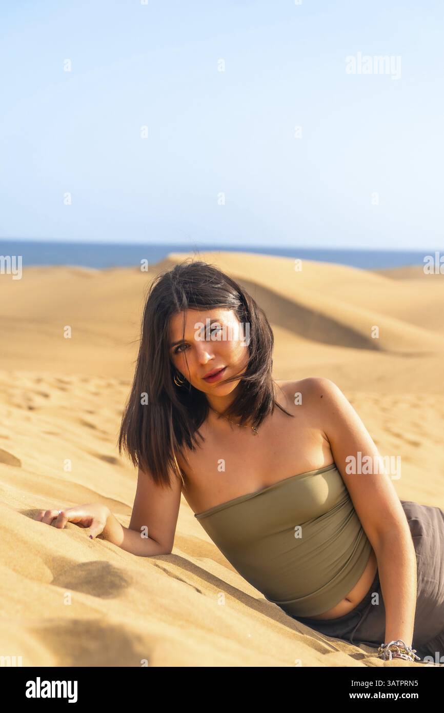 Giovane donna sdraiata sulla sabbia tra le dune di maspalomas, gran canaria, isole canarie, spagna, che gode di vacanze estive Foto Stock