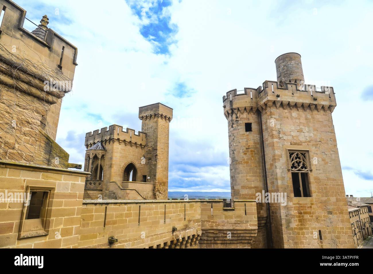 Maestose torri medievali e mura che si innalzano contro un cielo nuvoloso, mostrando la grandiosità architettonica del palazzo reale di olite in navarra, spagna Foto Stock
