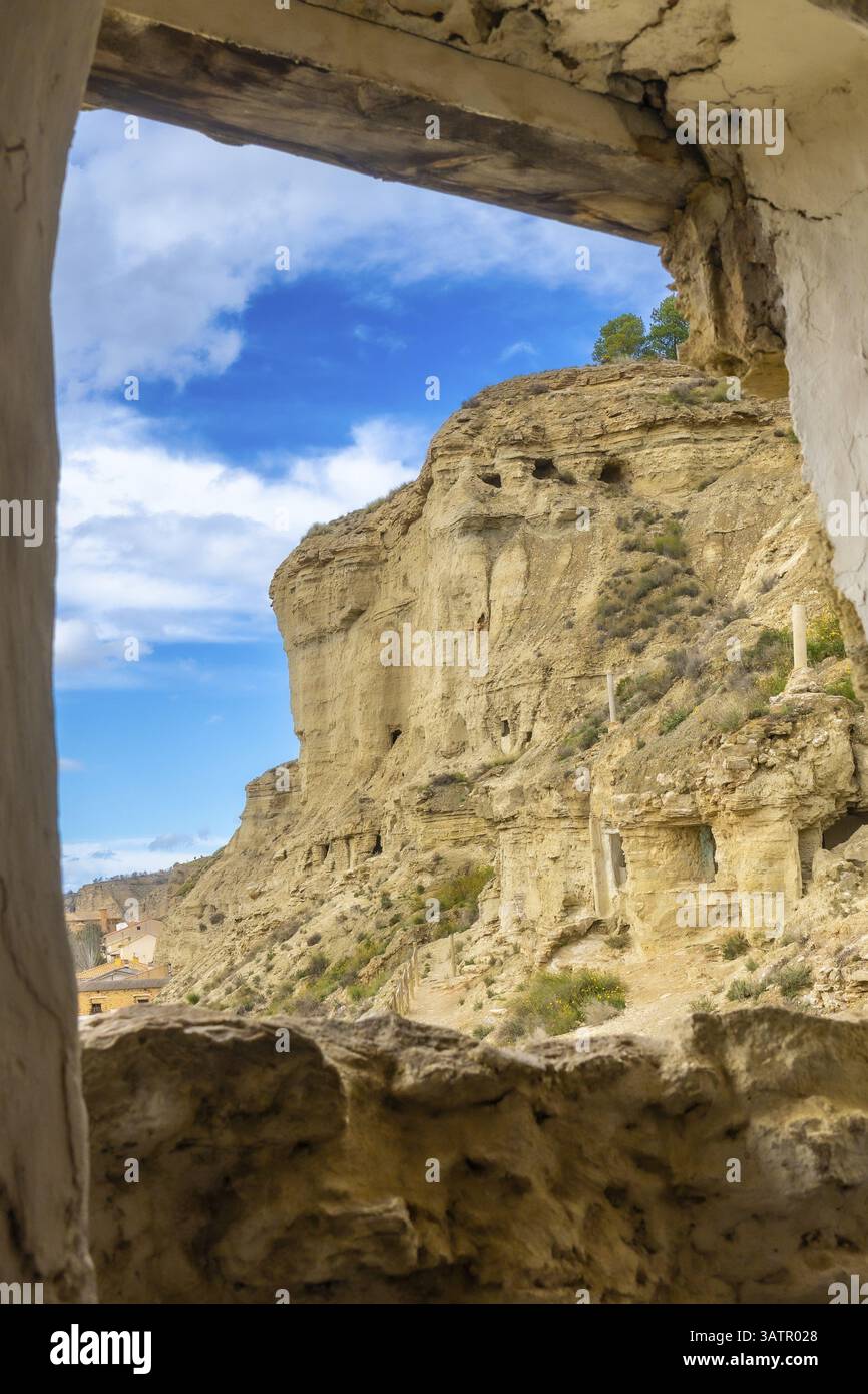 Scogliere di arenaria con abitazioni in grotta che si affacciano sul villaggio di arguedas in navarra, spagna, viste da una vecchia finestra Foto Stock