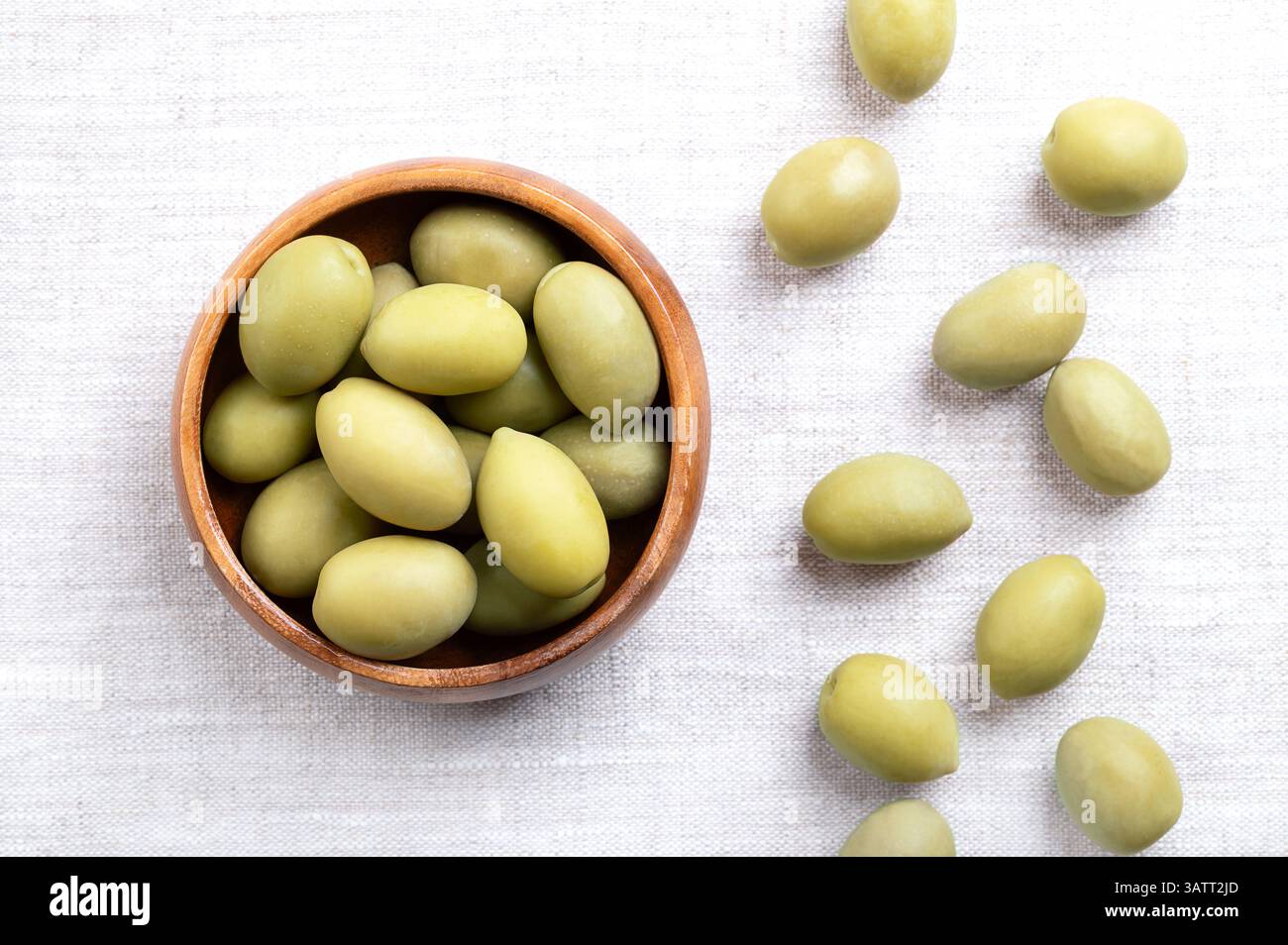 Olive verdi con buco, in una ciotola di legno su lino. Olive da tavola grandi e intere, raccolte prima di essere completamente mature, con un sapore più piccante e salato. Foto Stock