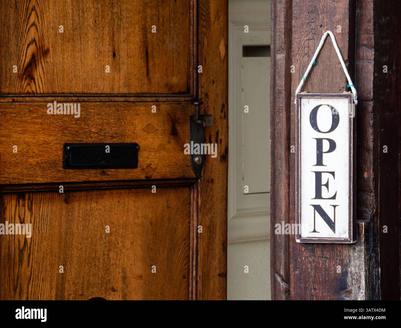 Una porta di legno leggermente socchiusa con un cartello APERTO appeso su di essa. Foto Stock