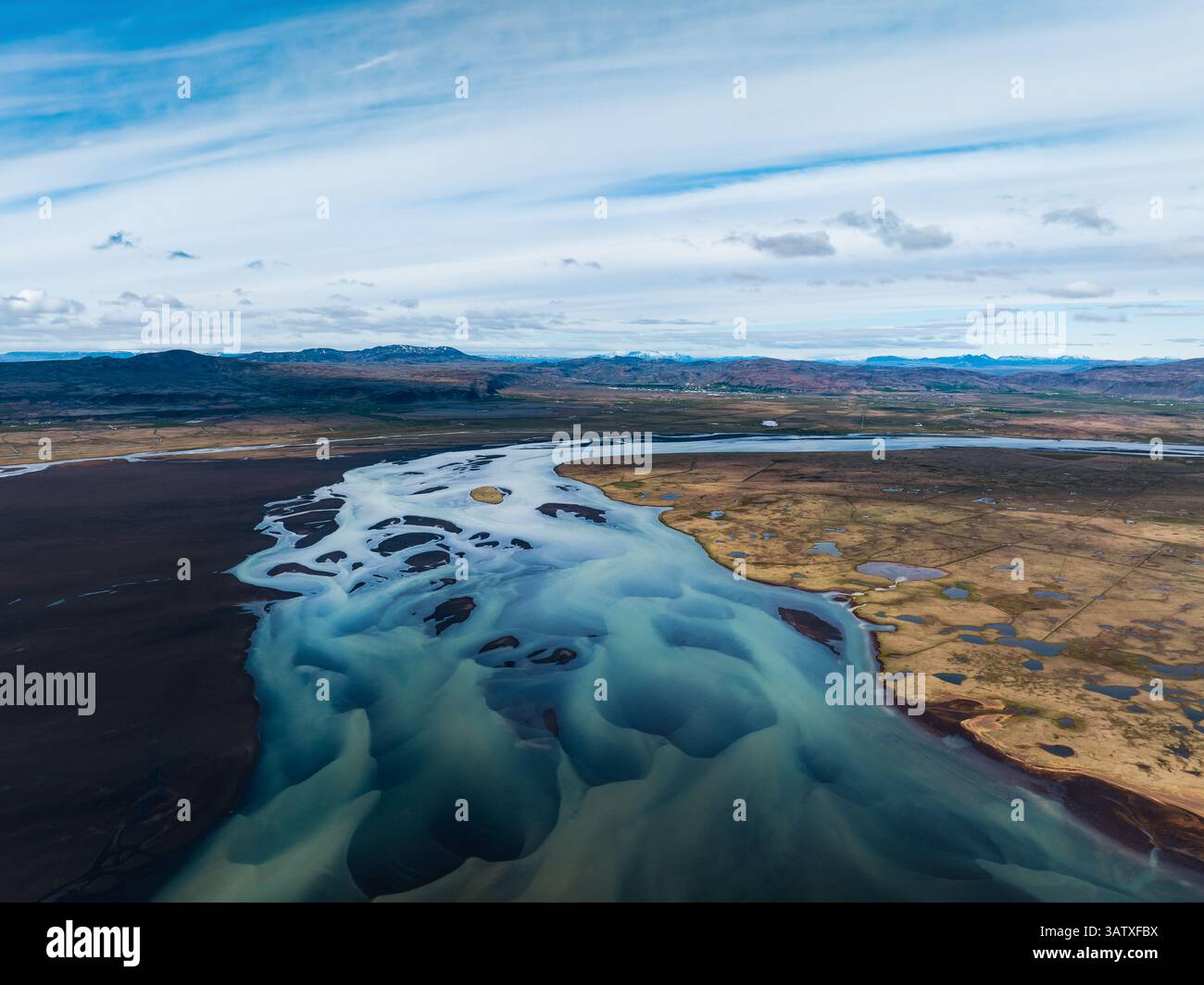 Ampia antenna di un fiume glaciale intrecciato che scorre attraverso le pianure islandesi sotto un cielo blu, mostrando canali tortuosi. Foto Stock