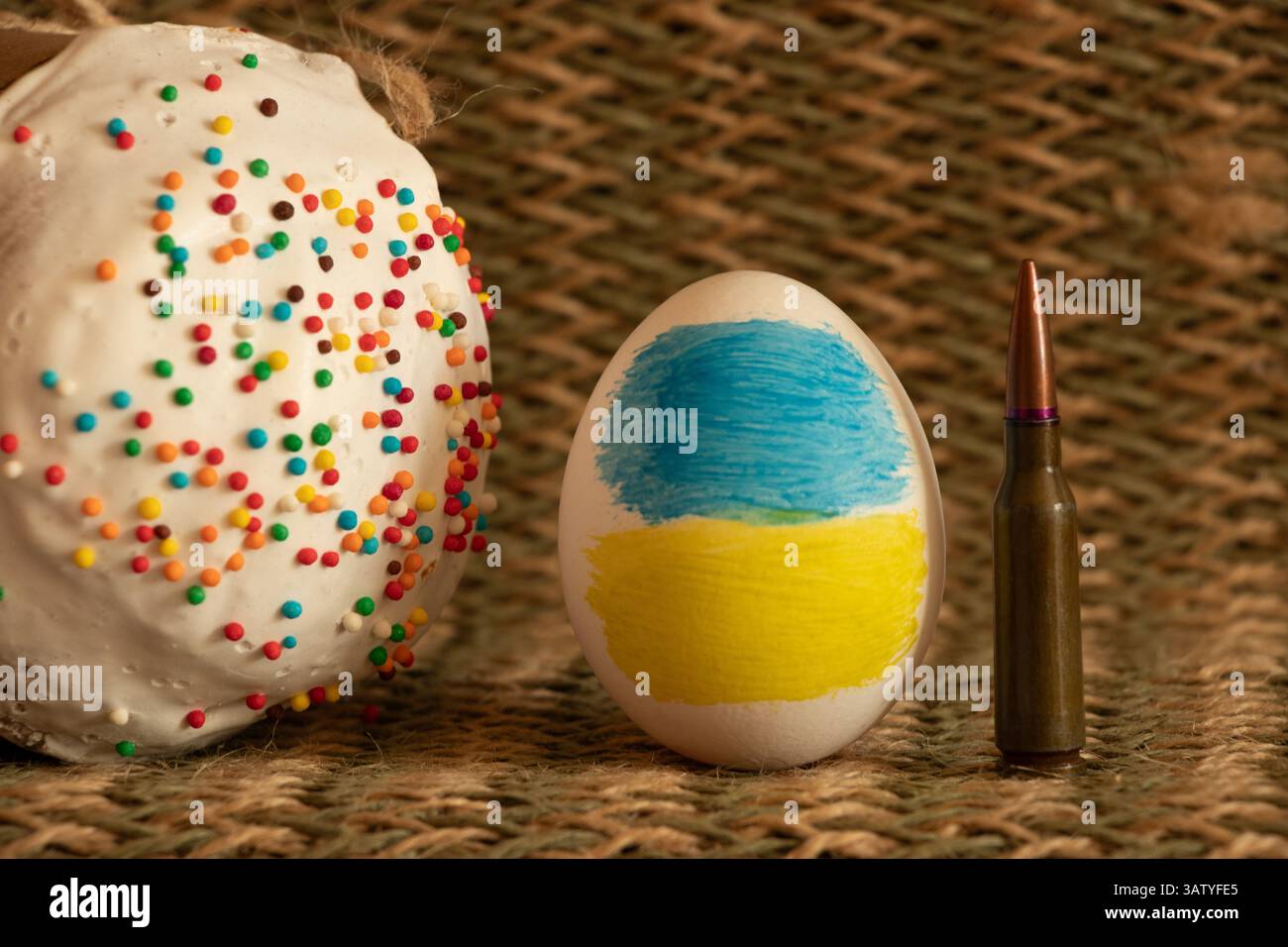Una bandiera Ucraina dipinta su un uovo di Pasqua, e accanto ad esso Pasqua e un proiettile su una tovaglia di paglia, Pasqua in Ucraina in guerra Foto Stock