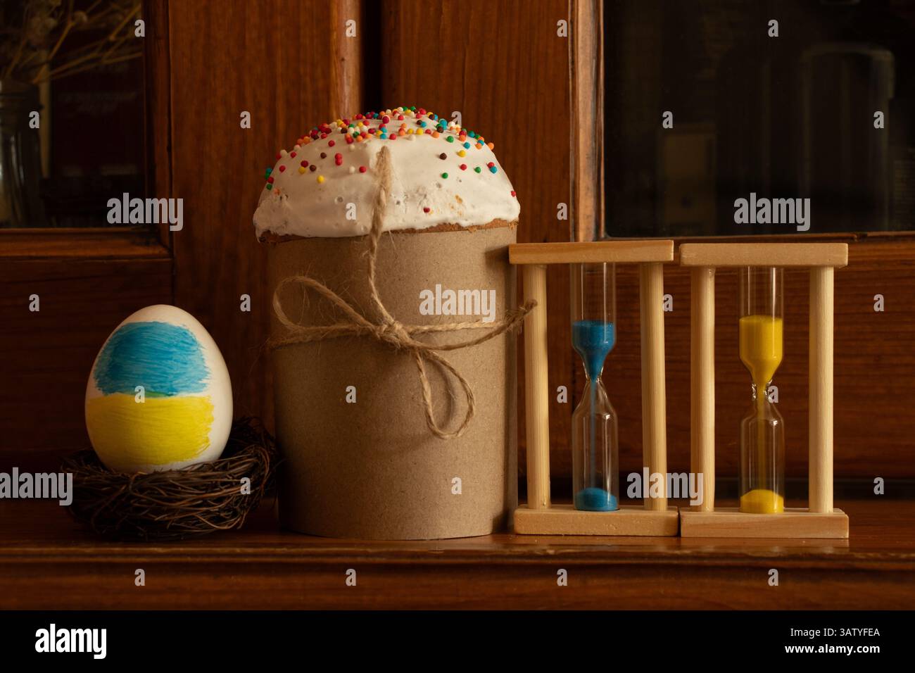 Torta di Pasqua con un uovo dipinto nei colori della bandiera Ucraina e una clessidra su un armadietto di legno, Pasqua in Ucraina e tempo Foto Stock