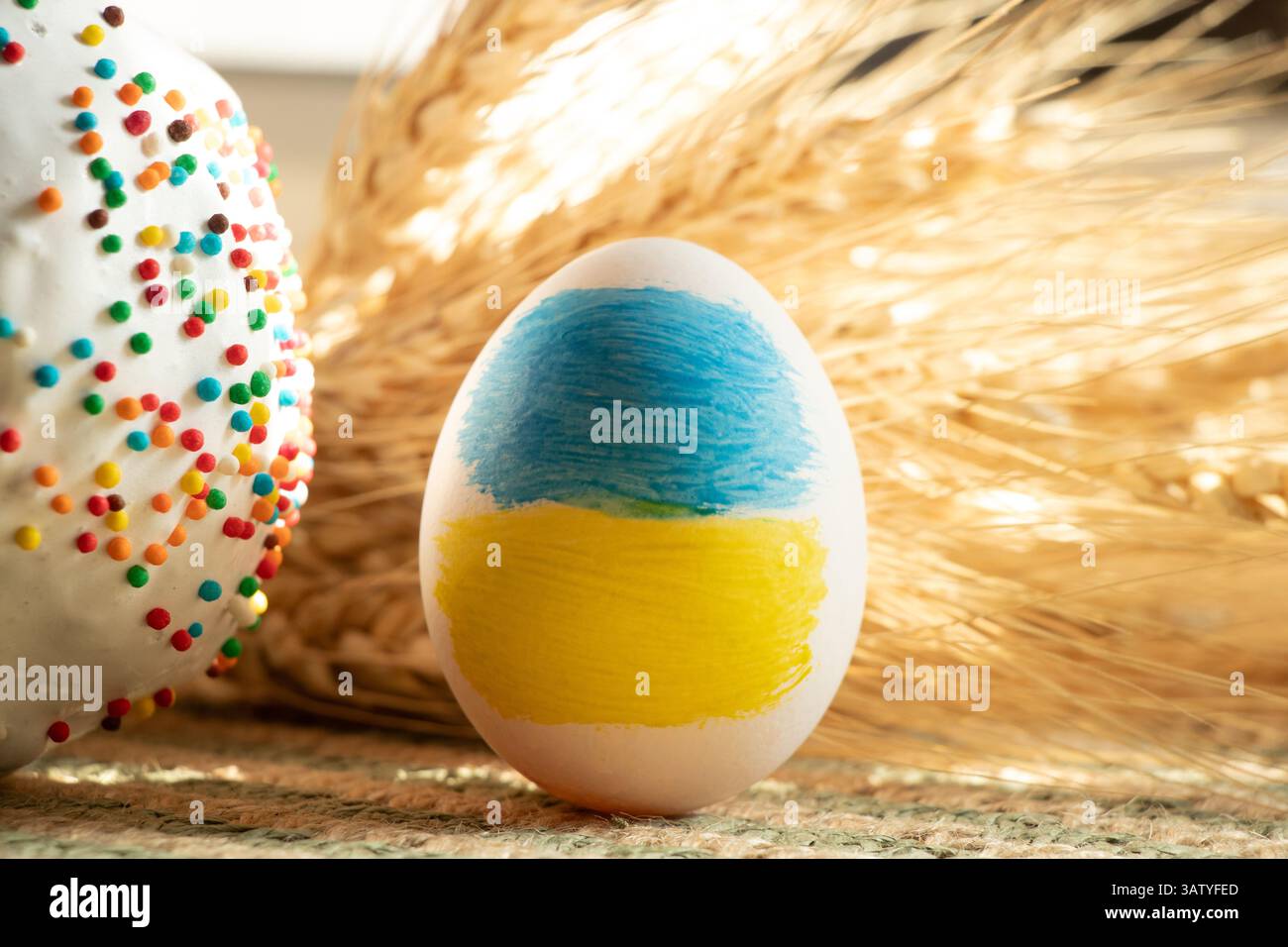 Dipinse la bandiera Ucraina sull'uovo di Pasqua, e accanto ad esso Pasqua e orecchie di grano al sole su un piatto di paglia, Pasqua in Ucraina Foto Stock