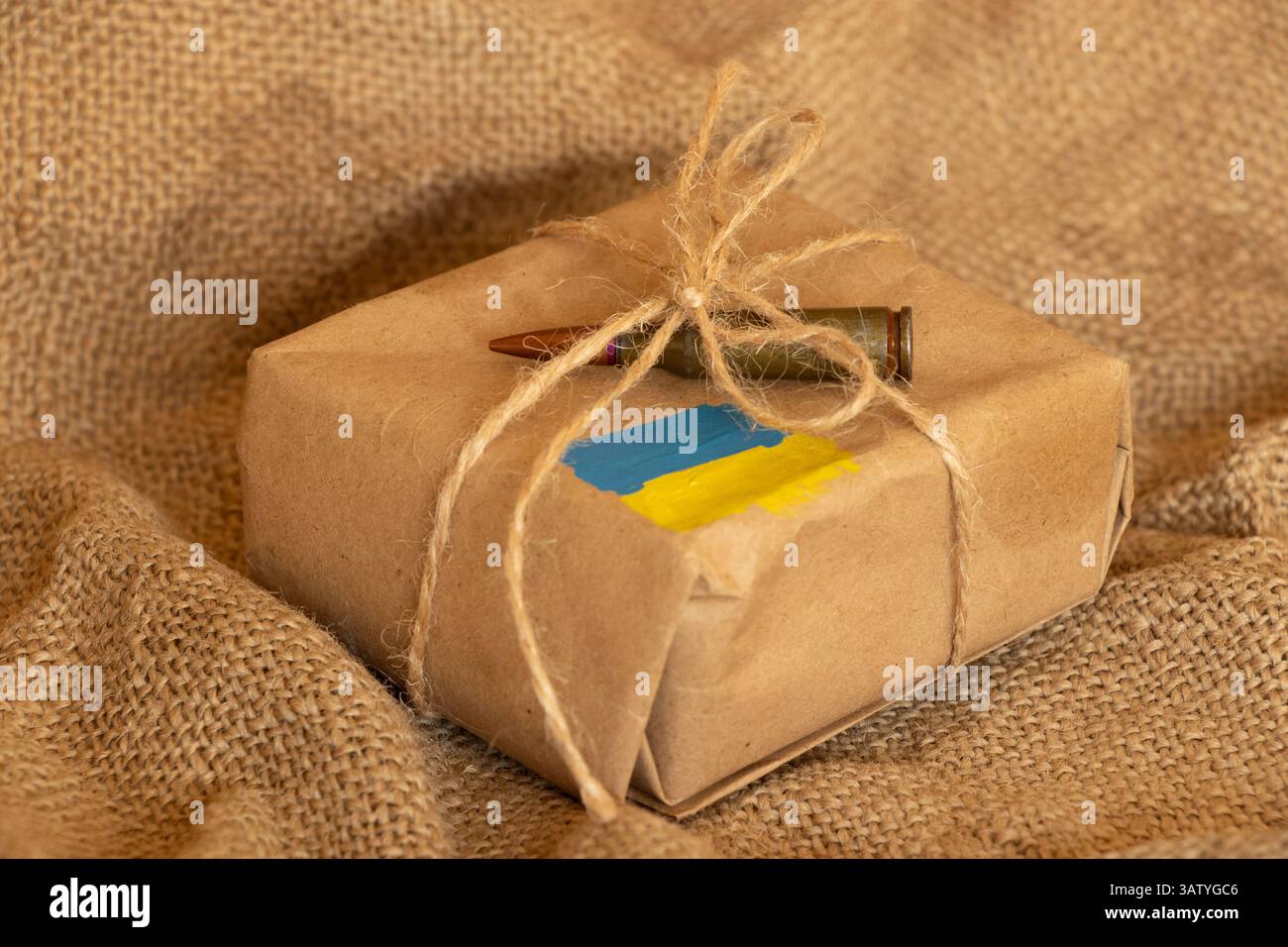 Una scatola regalo con una bandiera Ucraina dipinta e una pallottola giace su una scatola su uno sfondo di burlap, aiuti militari per l'Ucraina Foto Stock