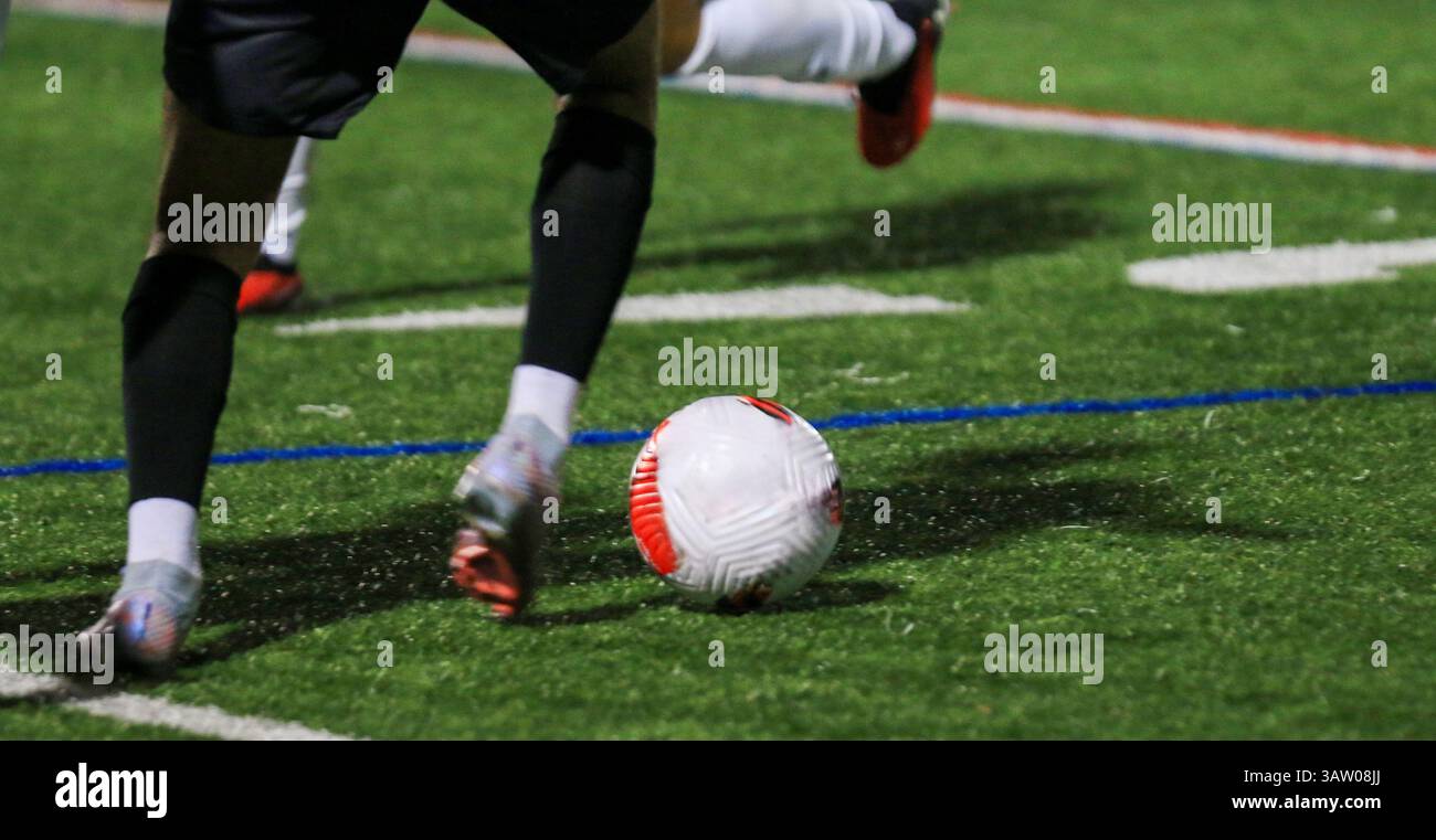 Il giocatore manovra abilmente la palla su un campo artificiale in erba durante una partita notturna. Foto Stock