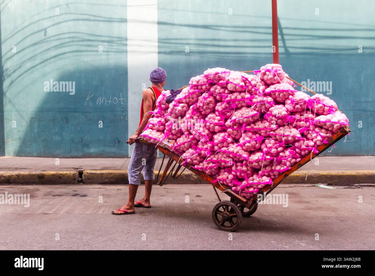 Un operaio filippino trasporta diversi sacchi pieni di aglio attraverso le strade trafficate di Manila, Filippine Foto Stock