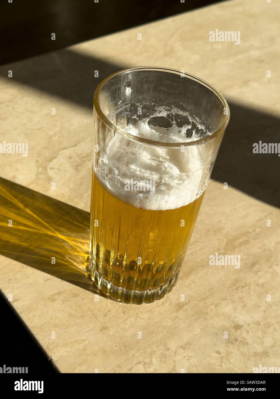 un bicchiere di birra semibevuto su un tavolo illuminato dal sole Foto Stock