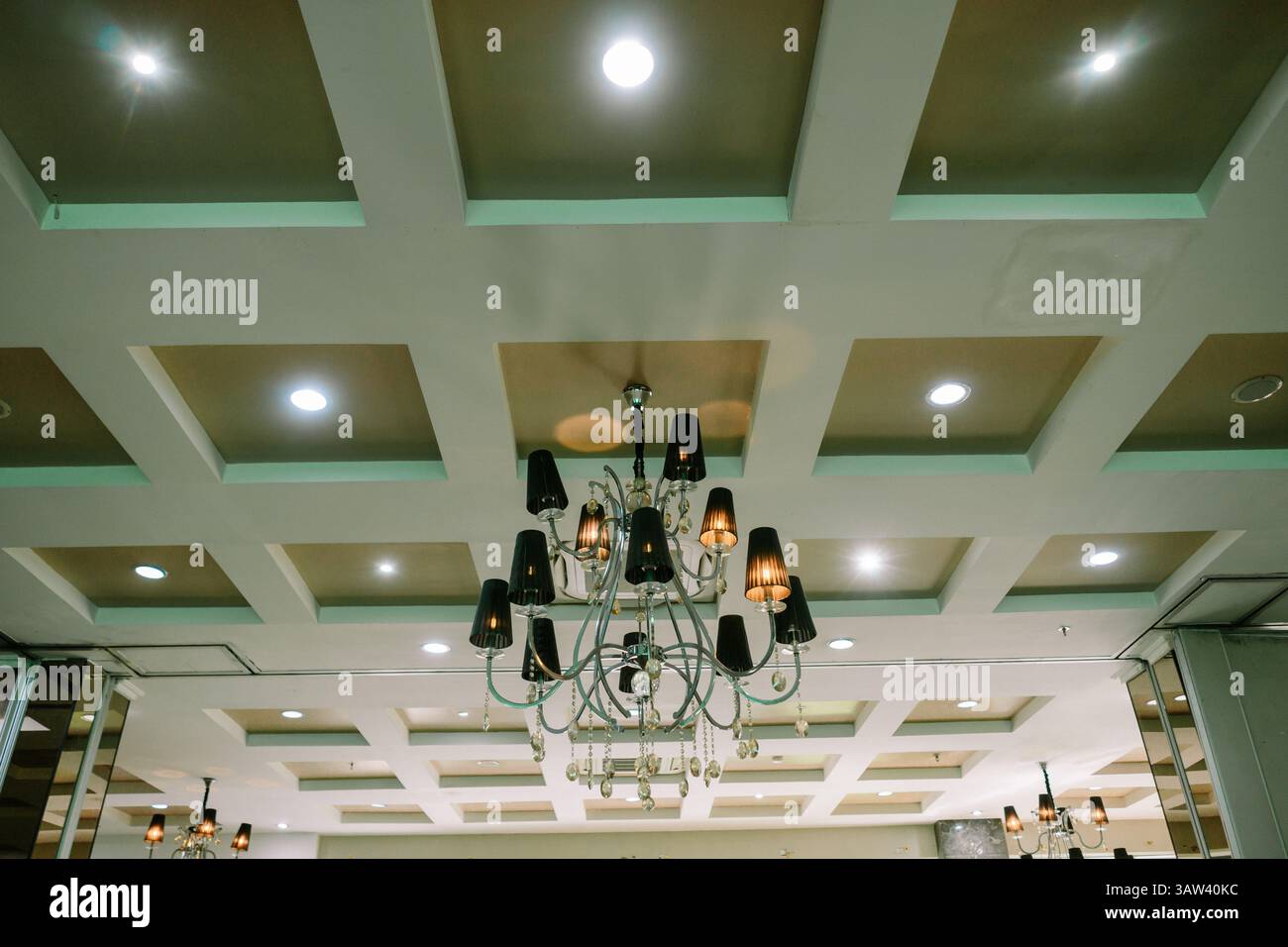 Elegante lampadario sullo sfondo del soffitto a cassettoni con pannelli quadrati e luci da incasso. Elemento di design degli interni. Foto Stock