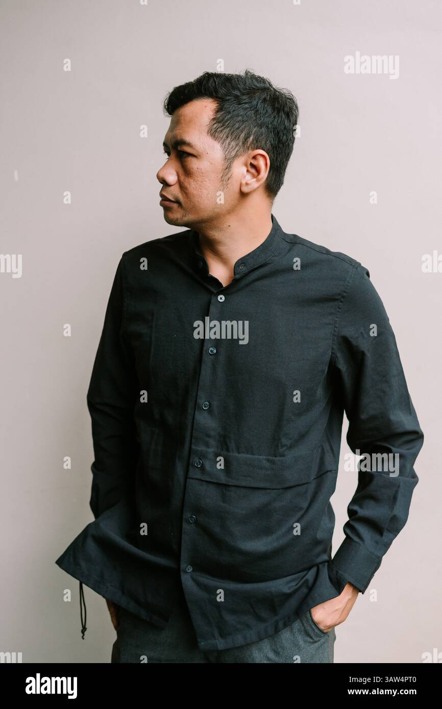 Un uomo premuroso in un abbigliamento casual guarda da parte. Ritratto di un uomo serio in piedi di fronte a uno sfondo semplice Foto Stock
