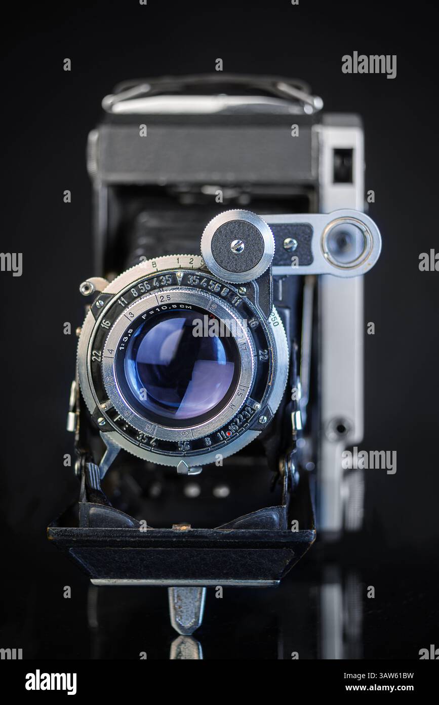 Una fotocamera vintage ripiegata con un obiettivo dettagliato è esposta in modo prominente su uno sfondo scuro, evidenziandone il design elegante e la meccanica. Foto Stock