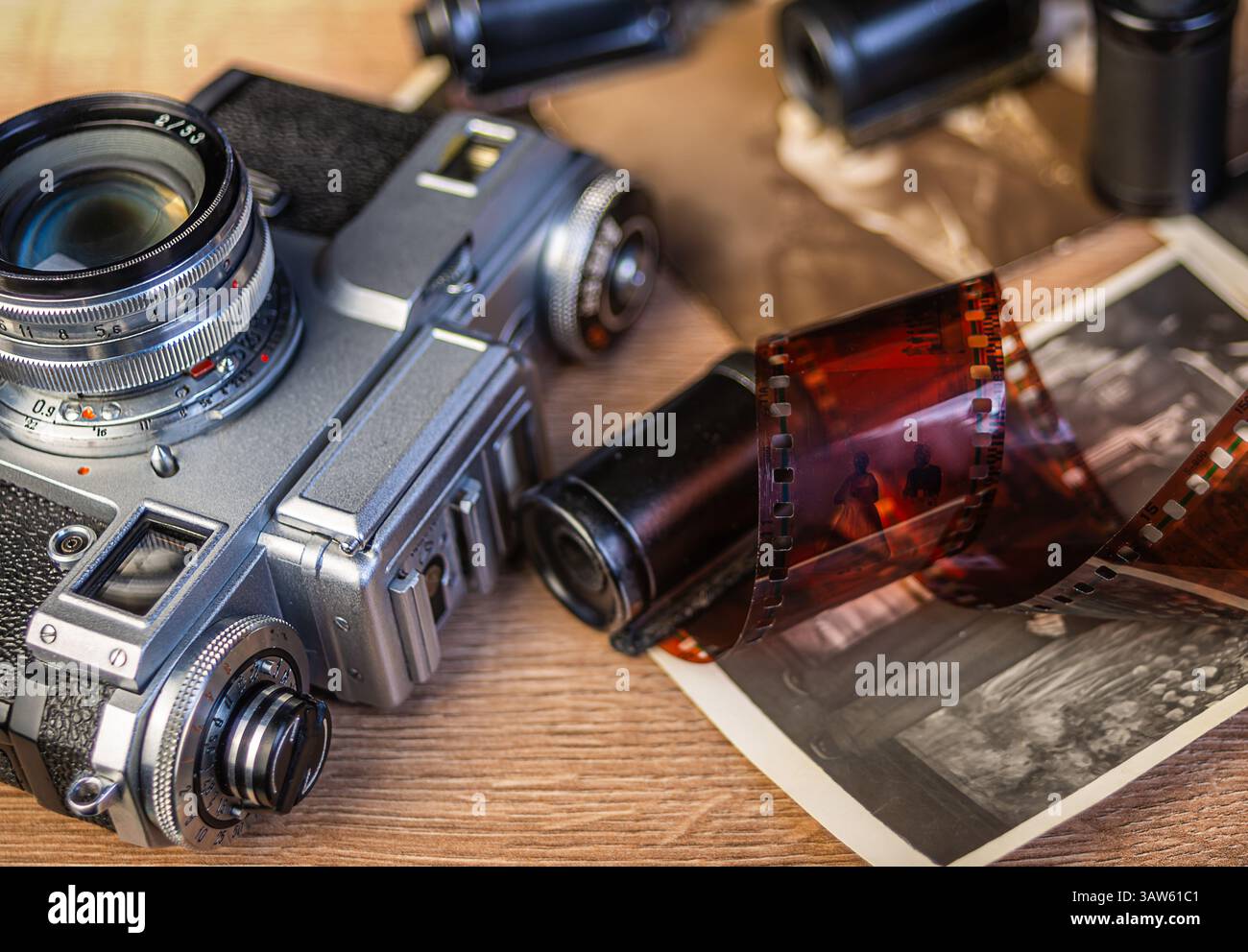 Una macchina fotografica d'epoca poggia su una superficie di legno circondata da fotografie in bianco e nero e rotoli di pellicola, evocando nostalgia per la fotografia classica. Foto Stock