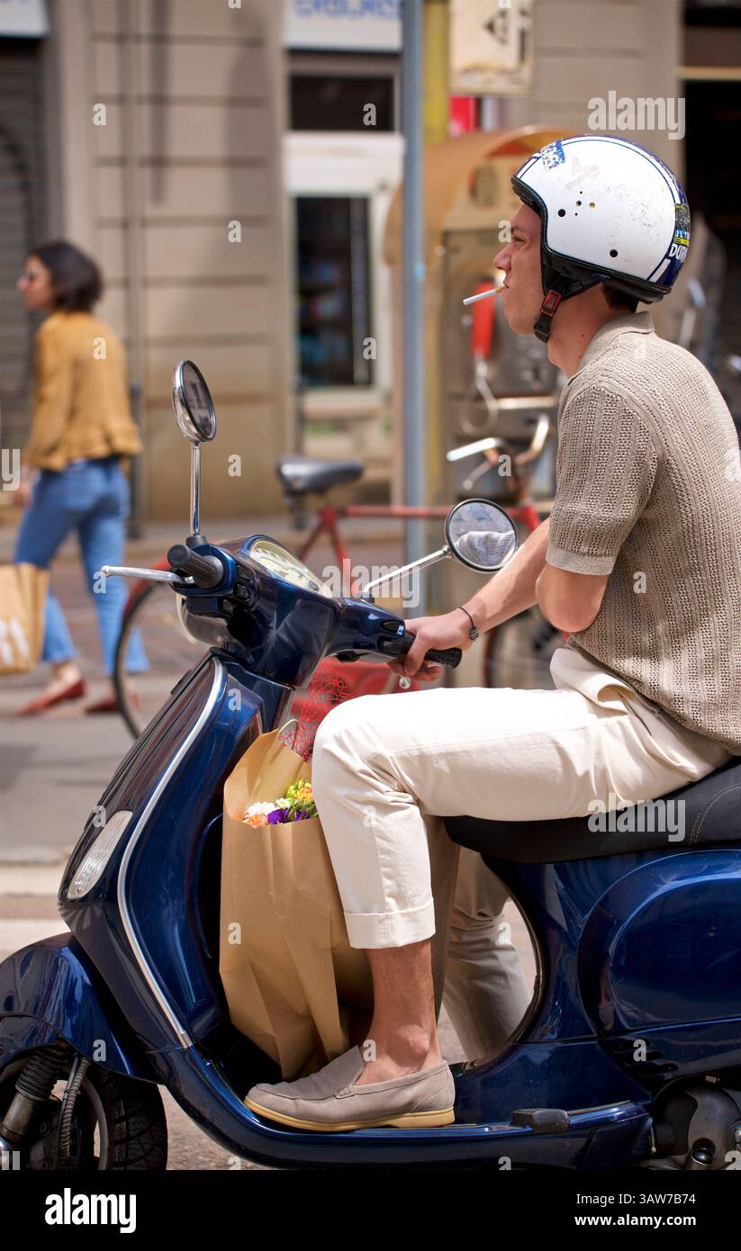 Giovane che fuma una sigaretta mentre guida una Vespa nel centro di Milano. Milano, Italia Foto Stock
