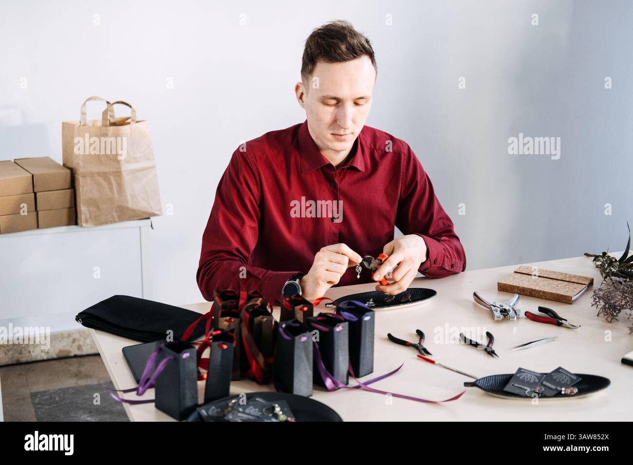 Designer indipendente di gioielli che realizza un orecchino personalizzato su un tavolo pieno di strumenti e confezioni regalo. Gioielli personalizzati, regali su misura, emozionali Foto Stock