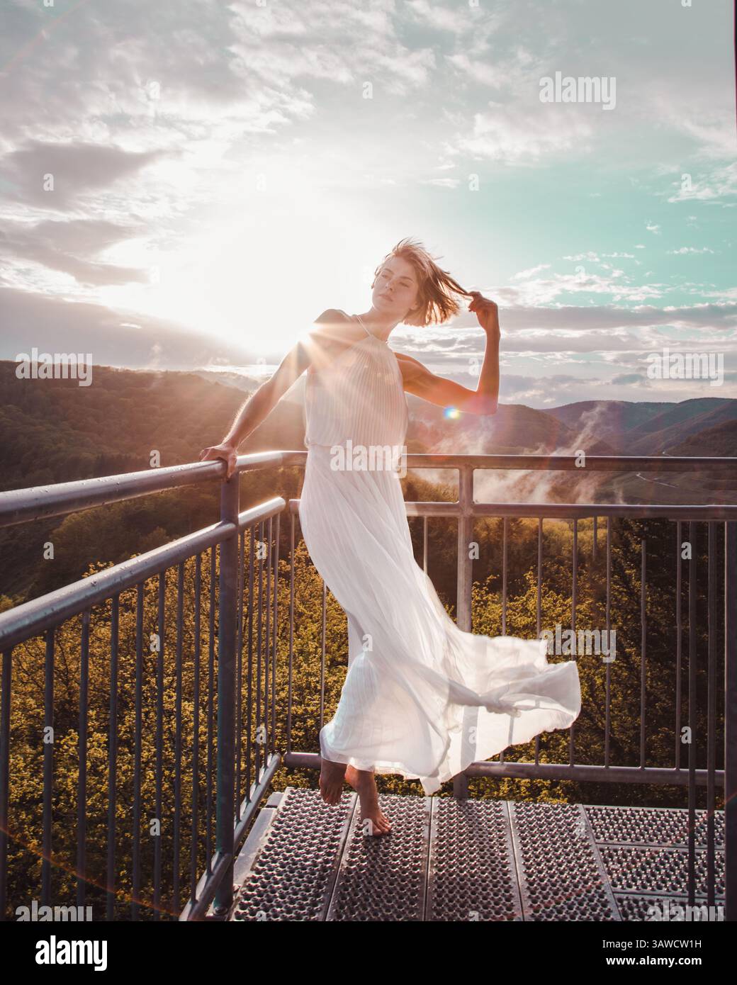 Bella donna in abito bianco che abbraccia il bagliore dorato del sole del tramonto sulla torre panoramica 'Prinzenkopf' sul fiume Mosella in Germania. Foto Stock