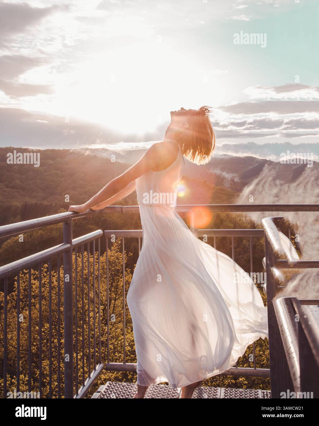 Bella donna in abito bianco che abbraccia il bagliore dorato del sole del tramonto sulla torre panoramica 'Prinzenkopf' sul fiume Mosella in Germania. Foto Stock