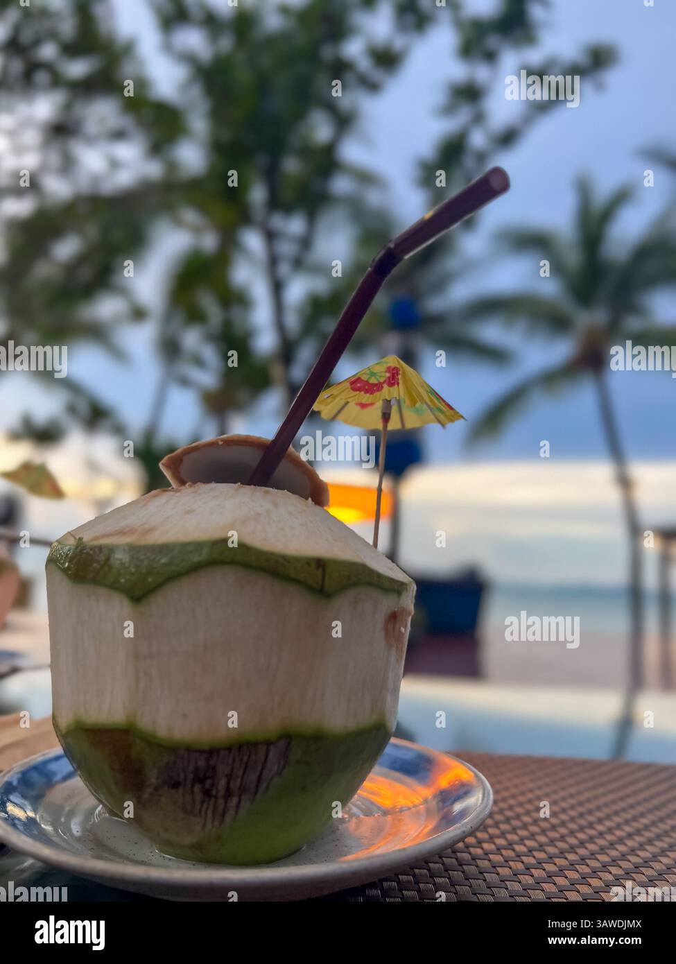 Bevanda fresca di cocco condita con un ombrello colorato e servita con una paglia, incarnando l'essenza di un paradiso tropicale. Foto Stock