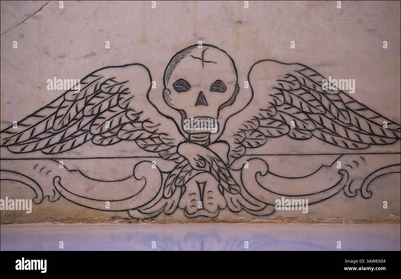 L'immagine mostra un disegno di un cranio alato, identificato come simbolo spesso visto in Puglia, Italia, in particolare su lapidi e in contesti religiosi. Questo motivo rappresenta la mortalità e la natura transitoria della vita. La Puglia, una regione dell'Italia meridionale, ha una ricca storia e cultura e tali simboli fanno parte del suo patrimonio artistico e religioso. Chiesa intagliata, Nardo, Puglia, Italia Foto Stock