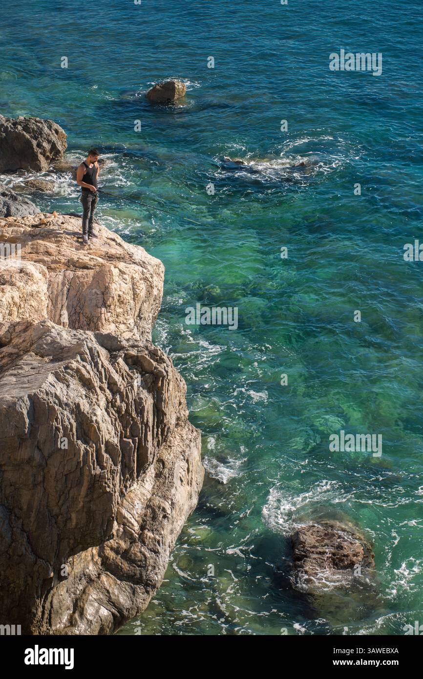 Uomo italiano con canna da pesca, stendingon una roccia e pesca nelle limpide acque blu del Golfo di Genova. Spiaggia di Varigotti. Varigotti è una frazione del comune di finale Ligure, in Liguria. Foto Stock