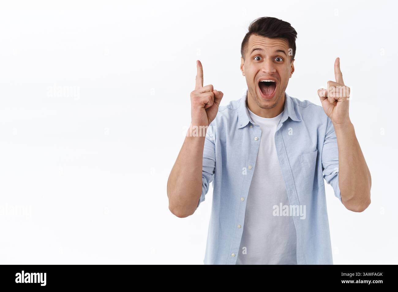 Ritratto di eccitato, gioioso e impressionato bell'uomo caucasico che punta le dita in su e sorridente ampiamente macchina fotografica, mostrando grande offerta, super miglior prezzo Foto Stock