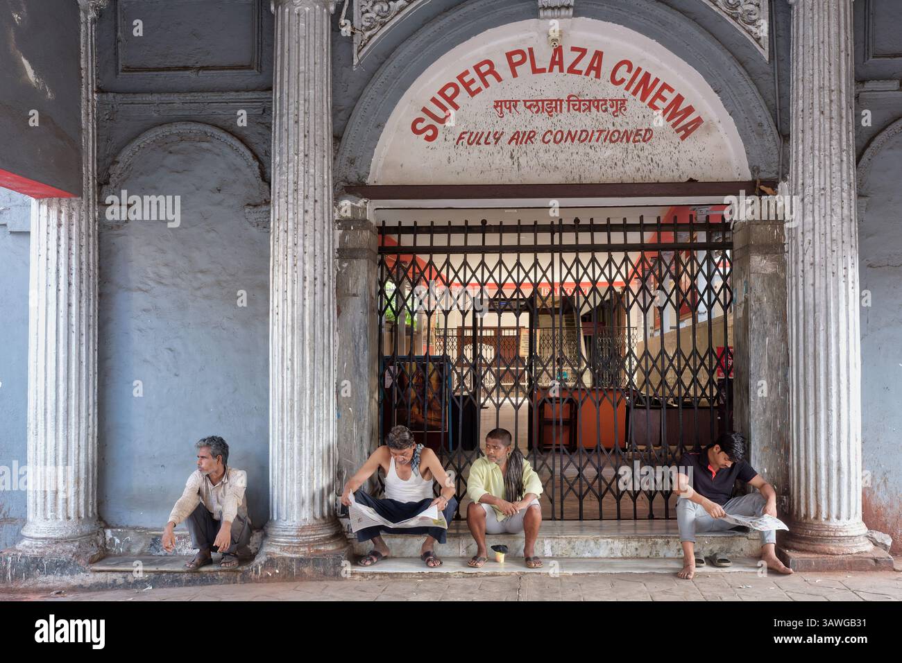 Uomini indiani seduti all'ingresso del Super Plaza Cinema, un cinema vecchio stile in Grant Road, Mumbai, India Foto Stock