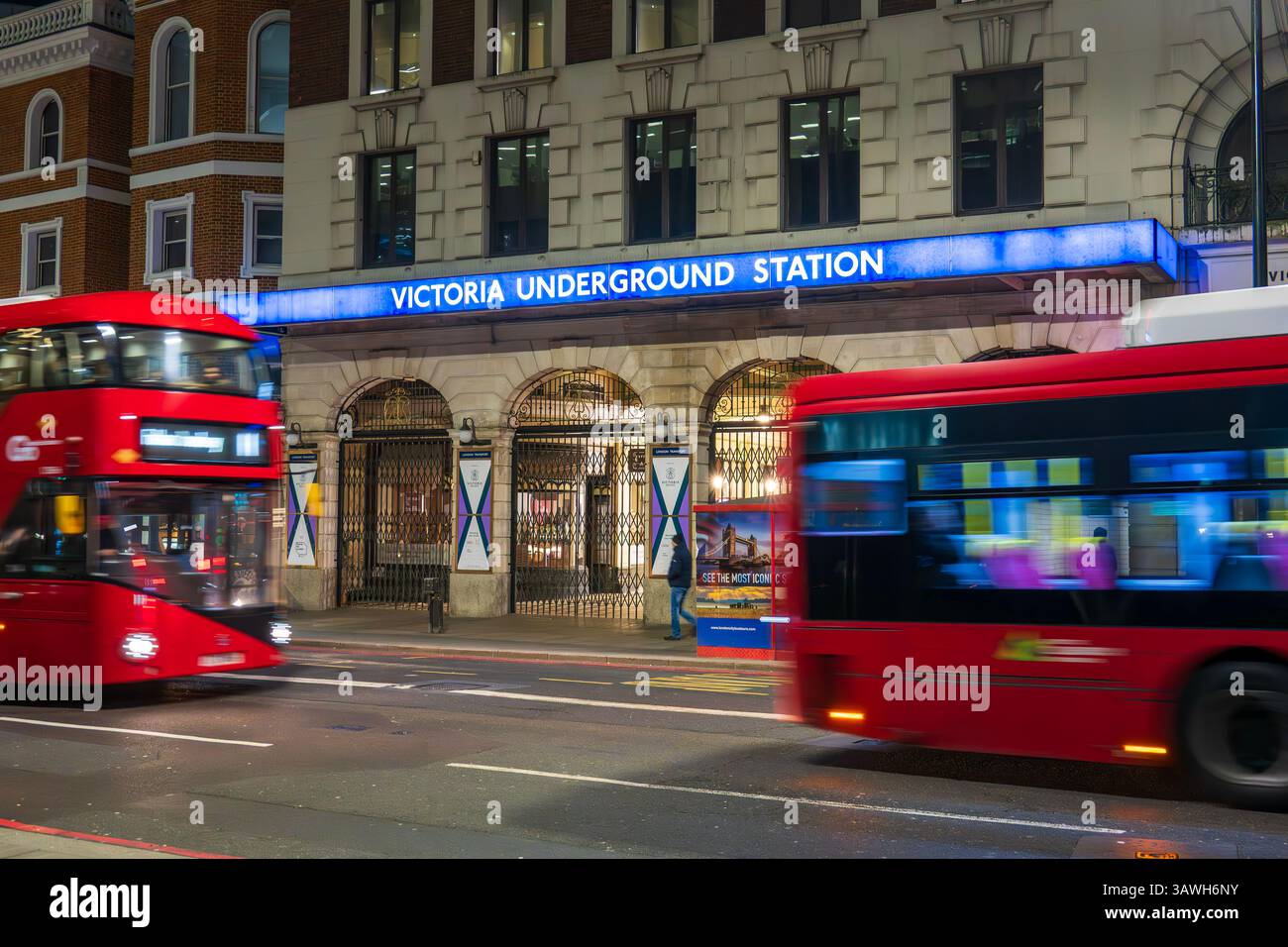 Ingresso alla stazione della metropolitana Victoria con autobus rossi di Londra che passano davanti all'ingresso di notte, Londra Foto Stock