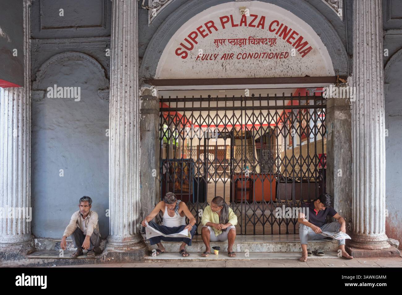 Uomini indiani seduti all'ingresso del Super Plaza Cinema, un cinema vecchio stile in Grant Road, Mumbai, India Foto Stock