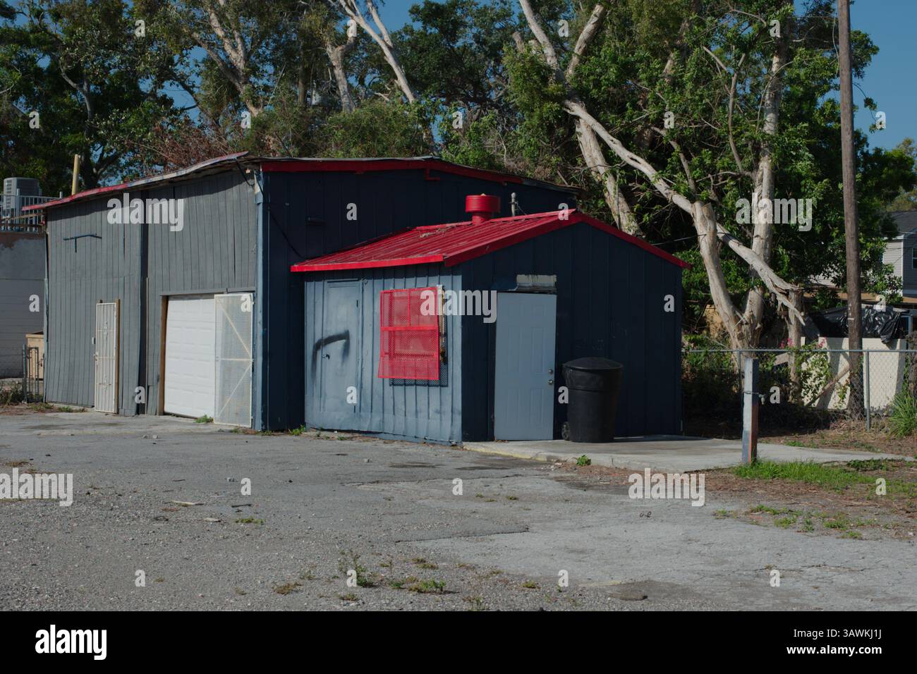Rustico edificio Garage in un tranquillo ambiente esterno circondato da alberi. Un pittoresco garage con tetto rosso e esterno blu si trova all'aperto, circondato da Foto Stock