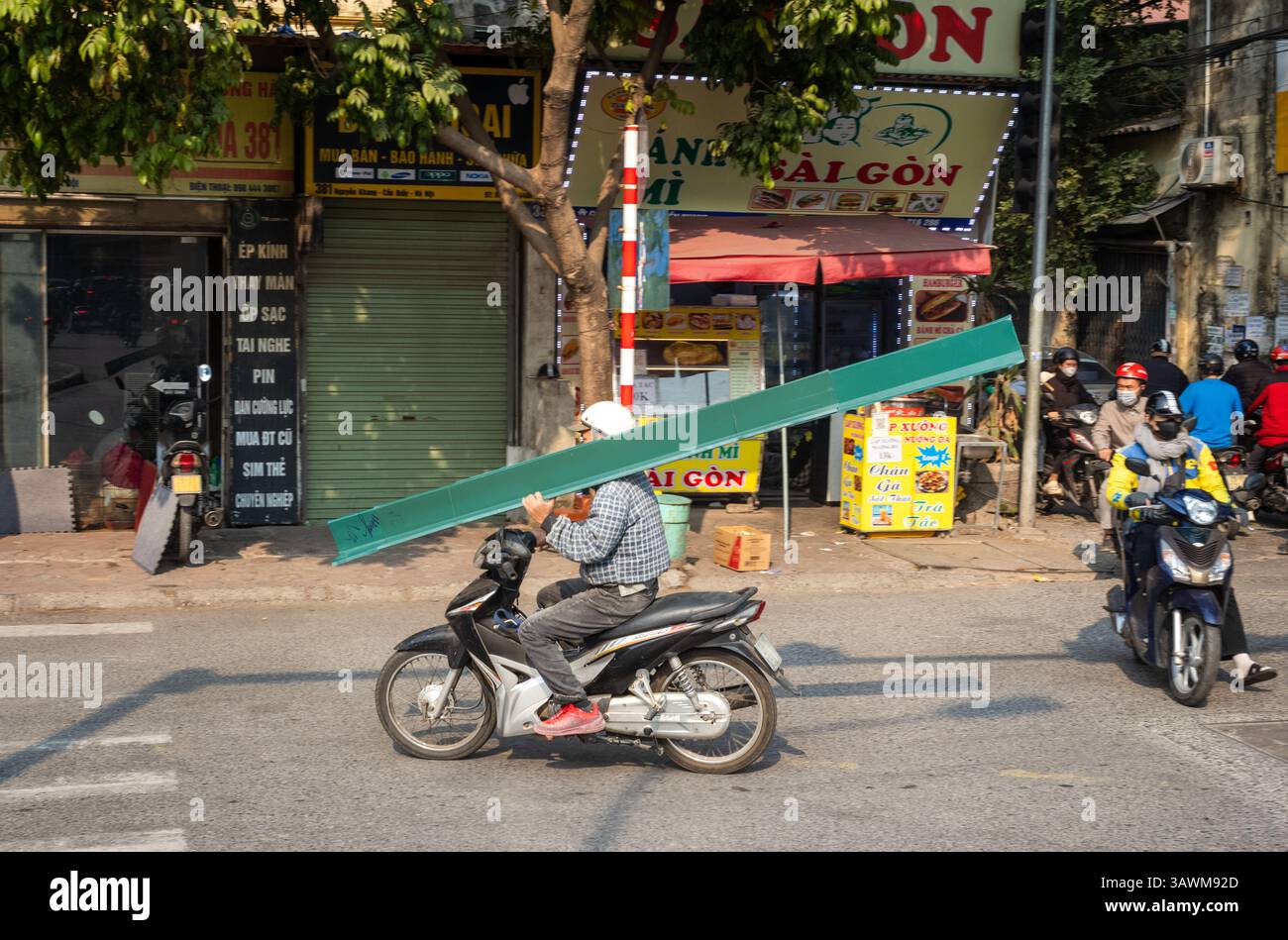 Un uomo porta lunghe lunghezze di plastica prefabbricata sulla spalla mentre guida la sua moto, Cau Giay, Hanoi, Vietnam Foto Stock