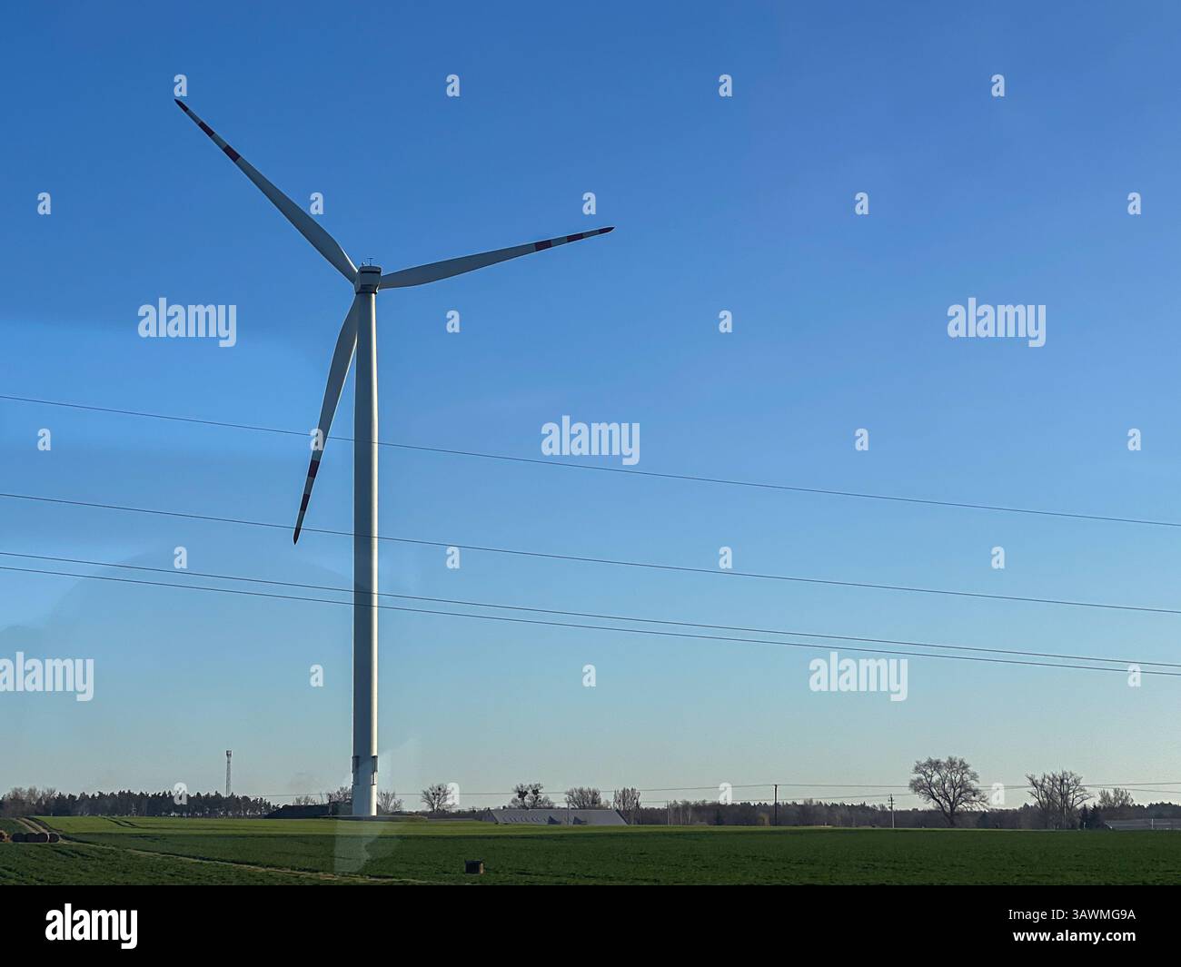 Una singola turbina eolica sorge sopra un campo verde in un'area rurale sotto un cielo azzurro. La scena mette in evidenza la produzione di energia rinnovabile e l'ambiente Foto Stock