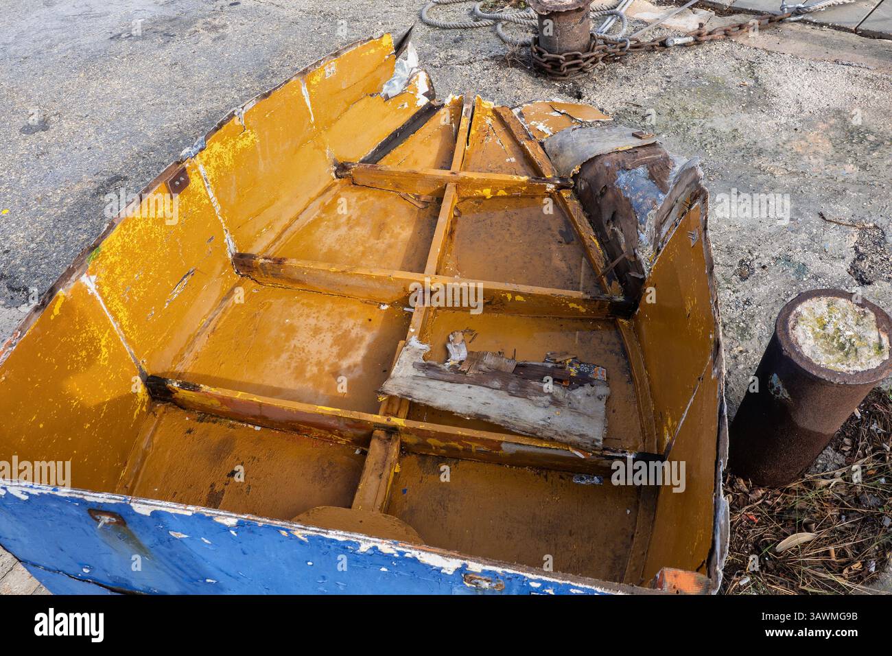 Vecchia barca in legno con pavimento aperto e prua gravemente danneggiata, nave nautica obsoleta lasciata su banchina di cemento. Foto Stock