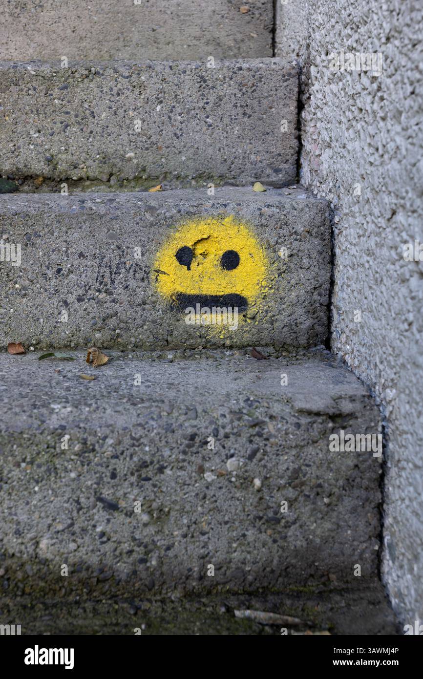 Emoji gialla su scale urbane in cemento, emoticon che mostra il volto neutro dritto, disinteressato, annoiato, nessuna espressione, indecisione, meh o senza espressioni Foto Stock
