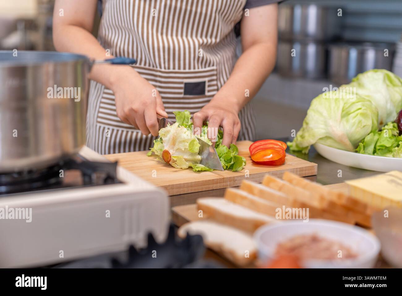 Primo piano di uno chef che taglia una testa di lattuga su un tagliere di legno in una cucina professionale. Lo chef indossa un grembiule a righe e un veget fresco Foto Stock