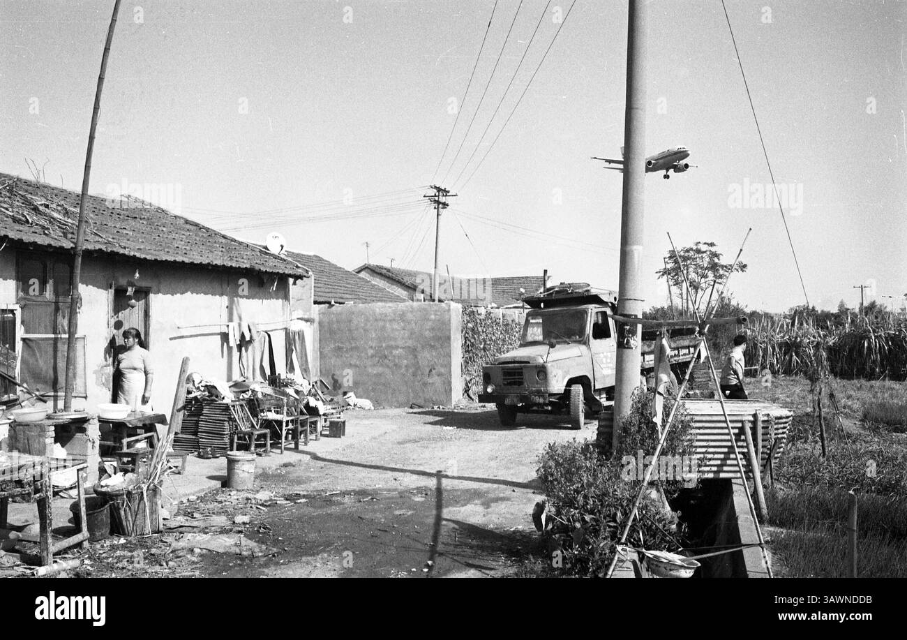 Vecchio quartiere animato dalla vita mentre un aereo si avvicina, catturando l'essenza delle routine quotidiane sotto il cielo espansivo: Low-Flying Airliner Over Rural Homestead vicino all'aeroporto di Hangzhou - Fotografia cinematografica d'epoca, anni '2000, Hangzhou, Zhejiang, Cina Foto Stock