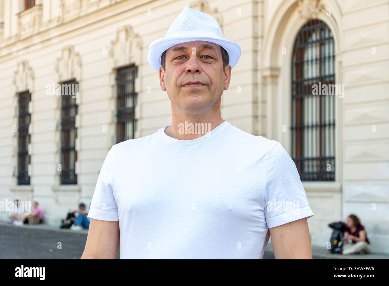 Ritratto di un uomo di 50-55 anni che indossa una t-shirt bianca e un cappello sullo sfondo di un edificio storico Foto Stock