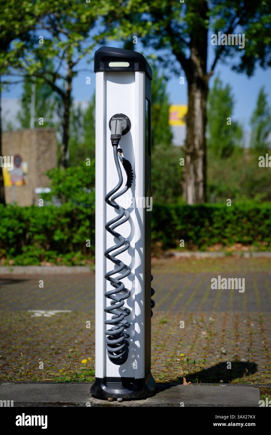 Stazione di ricarica bianca con cavo di ricarica leggermente danneggiato in un parcheggio vuoto su sfondo sfocato Foto Stock