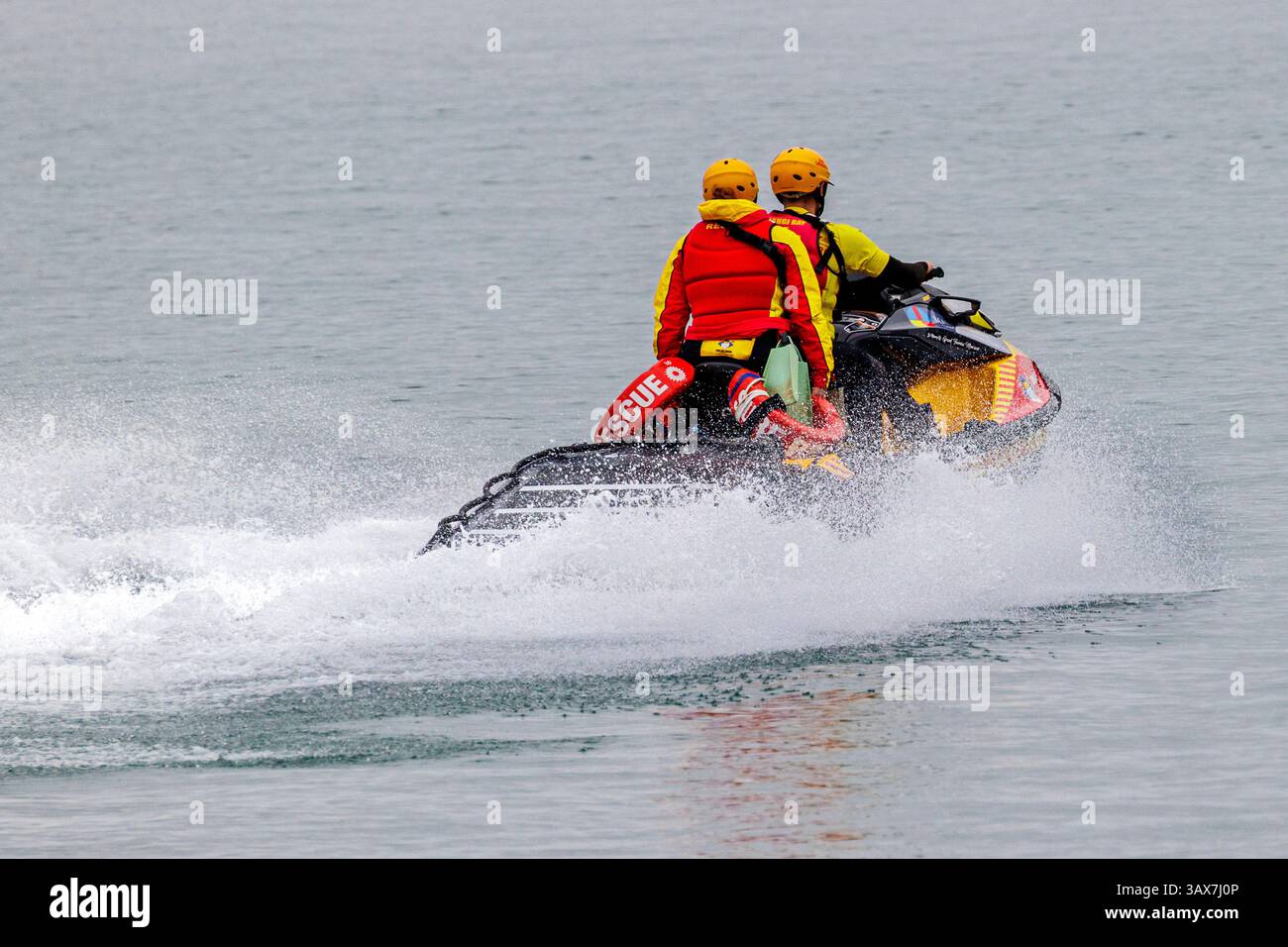 Due membri del team di salvataggio navigano su una moto d'acqua personale attraverso un tranquillo corpo d'acqua in un pomeriggio coperto Foto Stock