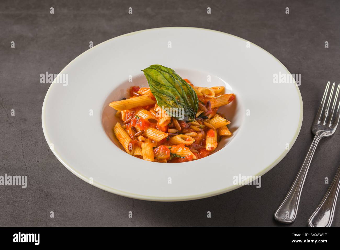 Penne alla arrabiata classica italiana con basilico e salsa su tavolo grigio scuro. Penne arrabbiata con salsa piccante Foto Stock