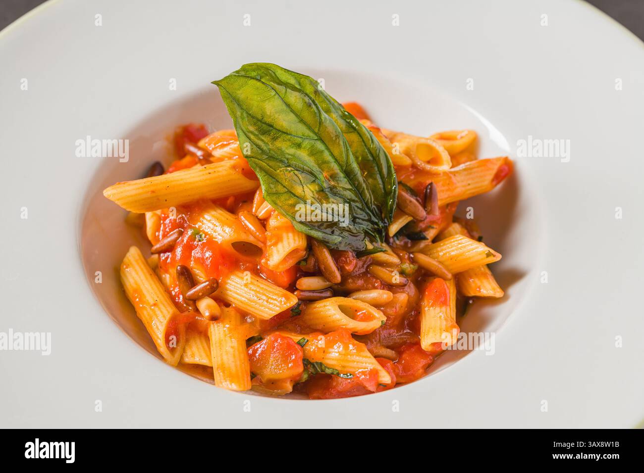 Penne alla arrabiata classica italiana con basilico e salsa su tavolo grigio scuro. Penne arrabbiata con salsa piccante Foto Stock