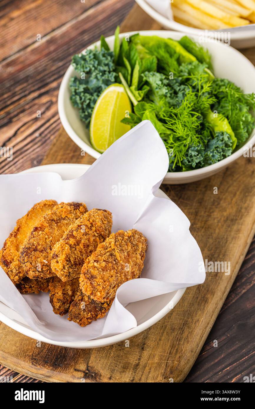 Ali di pollo croccanti con verdure e patatine fritte su un tavolo di legno Foto Stock