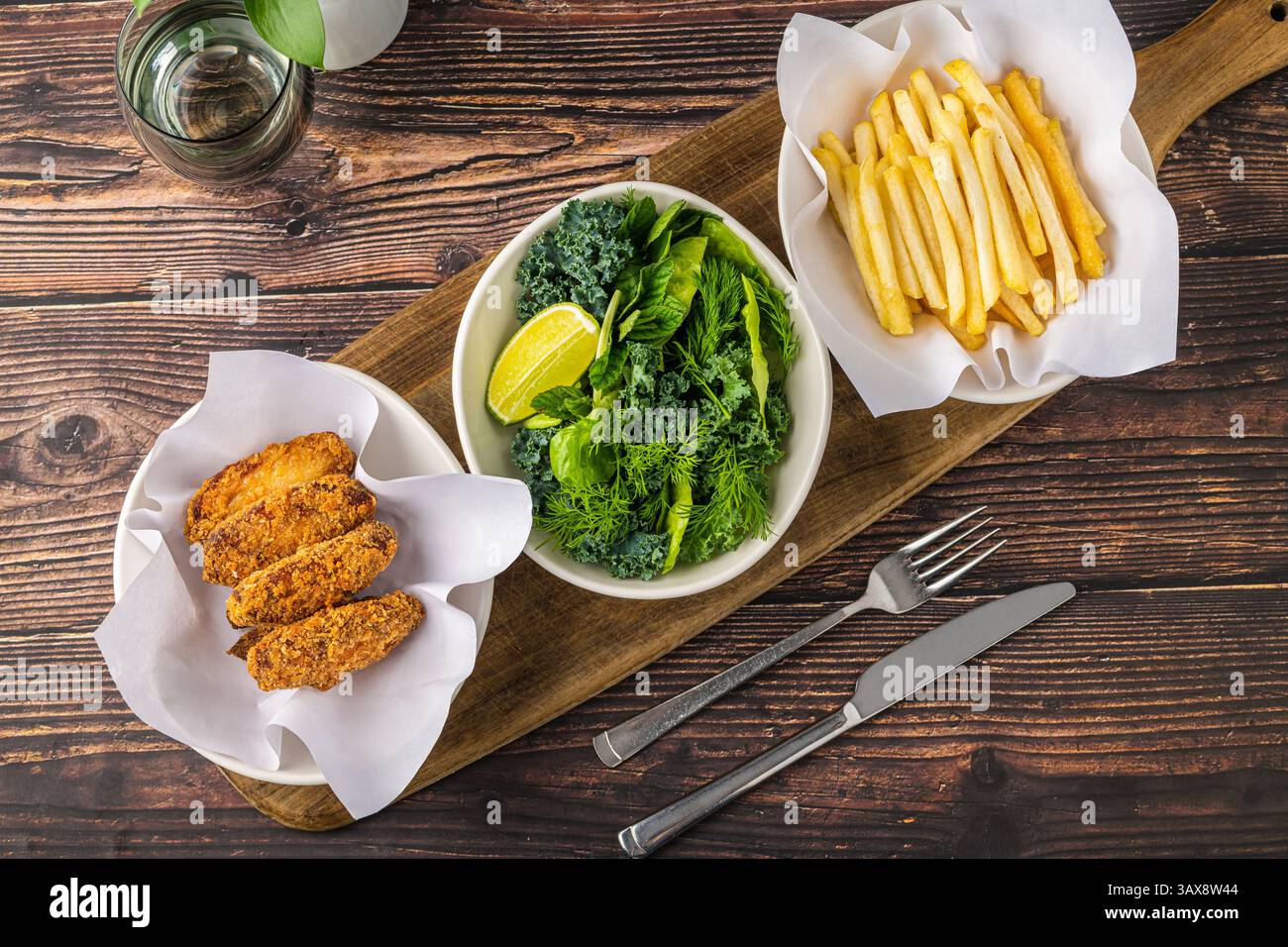 Ali di pollo croccanti con verdure e patatine fritte su un tavolo di legno Foto Stock