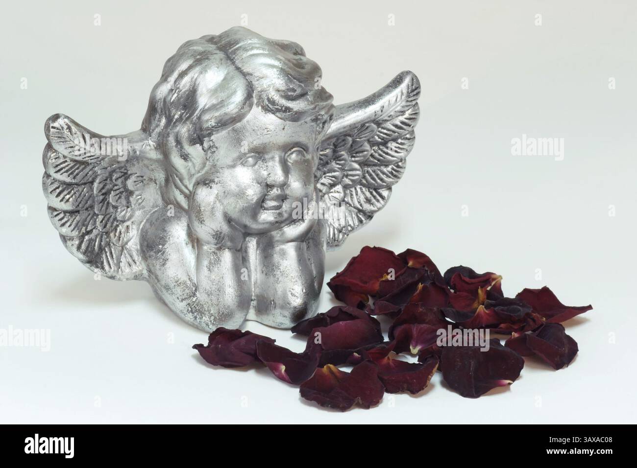 Statuetta d'angelo d'argento con petali di rosa su sfondo di colore chiaro Foto Stock