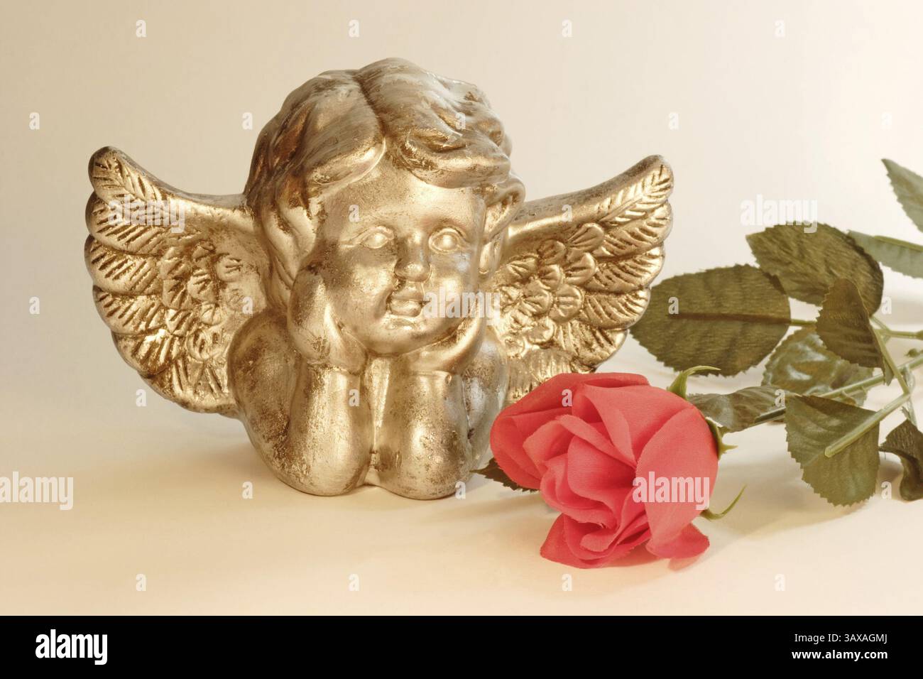 Angelo d'oro con una rosa rossa su sfondo di colore chiaro Foto Stock