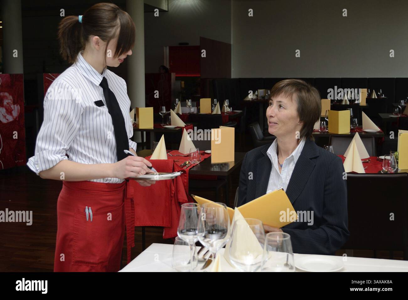 Un giovane specialista del ristorante prende l'ordine degli ospiti al tavolo Foto Stock